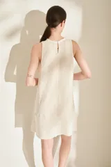 Vestido corto de lino italiano, sin mangas y con cuello redondo a la base. Presenta detalles desflecados en el cuello y costura central vertical.
