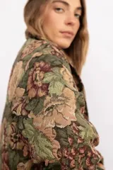 Campera tipo bomber con diseño de estampado floral estilo tapicería sobre fondo negro. Presenta cuello clásico, cierre frontal con botones metálicos, bolsillos laterales y puños elásticos.
