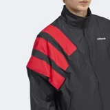 Campera deportiva Adidas de corte holgado, con cierre frontal de cremallera y cuello alto. Presenta un diseño en bloques de color negro con detalles en rojo en las mangas, confeccionada en tejido técnico reciclado.