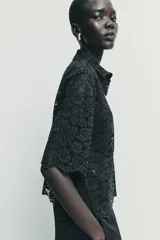 Camisa de encaje negro con cuello solapa, manga corta y cierre frontal con botones.