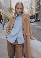 Abrigo largo de corte recto confeccionado en tejido mezcla de lana color camel. Presenta cuello con solapas de muesca, cierre frontal de doble botonadura, manga larga, un bolsillo de ribete en el pecho y dos bolsillos con solapa en la parte frontal. Incluye forro interior y abertura posterior en el bajo.