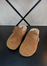Zuecos marrones con interior de corderito y hebilla lateral.