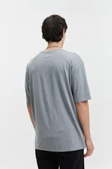 Remera de corte oversize color gris con efecto lavado, cuello redondo y mangas cortas. Presenta un estampado gráfico en color azul en la parte frontal superior.