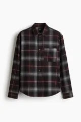 Camisa de franela de manga larga con cuello inglés, tapeta lisa, canesú en la espalda, bolsillo superior abierto y bajo redondeado. Presenta un patrón de cuadros en tonos negro, gris y granate.