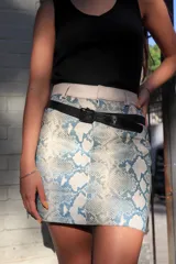 Minifalda con estampado de piel de serpiente en tonos celeste y blanco, con pretina ancha color crudo y cinturón fino negro.