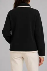 Saco de punto negro con cierre frontal, cuello tipo polo y detalles de ribete en color crema en el cuello, puños, ruedo y a lo largo del cierre. Cuenta con dos bolsillos laterales.