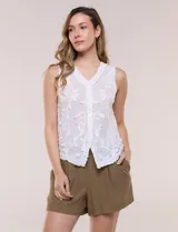 Blusa sin mangas blanca de puro algodón liviano, con escote en V, bordados florales en relieve, cartera frontal abotonada y terminaciones con festón calado.