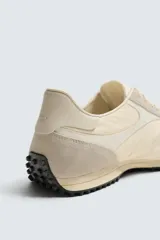 Zapatilla de estilo retro con cordones, confeccionada en tejido técnico y detalles de cuero con acabado serraje. Presenta suela dentada con contraste de color.