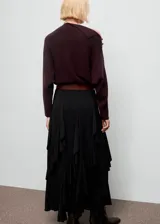 Jersey de punto color marrón oscuro, con diseño recto, cuello asimétrico y manga larga. Presenta detalle de botones efecto joya en el hombro.