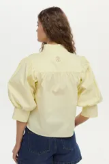 Camisa blanca de cuello mao con volados, mangas abullonadas y cierre frontal con botones.