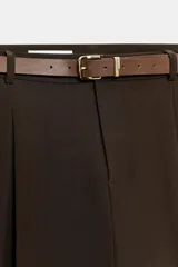 Pantalón tobillero de tiro medio, color beige, con pinzas delanteras y bolsillos frontales. Incluye un cinturón fino de cuero marrón con hebilla metálica dorada y cierre frontal con cremallera, botón interior y gancho.