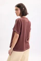 Camiseta marrón de manga corta holgada, con cuello redondo y costuras con pespuntes en color blanco contrastante en el dobladillo y las mangas.