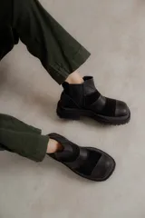 Botas de caña baja con punta cuadrada, confeccionadas en una combinación de cuero liso y gamuza. Presentan un diseño con múltiples cortes y costuras visibles, elásticos laterales y suela de goma tipo track con plataforma.