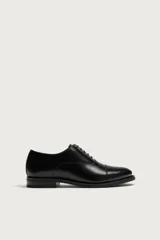 Zapato de vestir tipo derby fabricado en piel, con horma redonda y suela a contraste con ligero tacón.