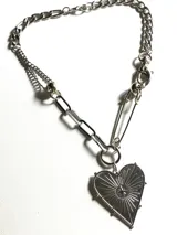 Collar de cadena de acero inoxidable con diseño asimétrico que combina eslabones gruesos y una cadena fina. Presenta un dije central en forma de corazón con grabado de rayos y una estrella, unido a la cadena mediante un gancho tipo imperdible.