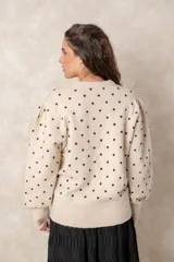 Buzo de punto color beige con estampado de lunares negros en relieve, cuello redondo y mangas largas abullonadas con puños acanalados.
