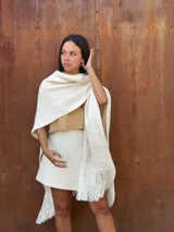Ruana tejida de lana en color crudo, con diseño de flecos en los bordes. Es una prenda versátil y abrigada, ideal para complementar diversos looks.