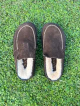 Zueco de cuero color marrón oscuro, con costuras decorativas en hilo rojo en el empeine y suela plana de goma.