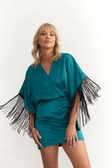 Vestido corto color verde esmeralda de satén, con escote cruzado, mangas cortas con flecos negros y falda drapeada con elástico en la cintura.