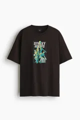 Remera de algodón marrón oscuro con cuello redondo y mangas cortas. Presenta un estampado frontal con gráficos de básquetbol y texto 'Street Hoops 95'.
