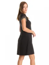 Vestido corto negro de seda fría, con escote redondo y mangas casquillo decoradas con perlas y tachas. El corte se ajusta levemente en el busto y se abre hacia el ruedo.