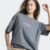 Remera de corte oversize color gris, con cuello redondo y mangas cortas. Presenta un estampado pequeño en el centro del pecho con motivos florales y de frutas en color rosado.