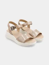 Sandalia de plataforma color beige, con tira ancha en el empeine con textura reptil brillante y tira ajustable con hebilla en el tobillo. La suela es blanca y gruesa.
