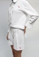 Short de tiro medio confeccionado en algodón tussor, de color blanco con costuras a la vista en color rojo. Presenta tablones delanteros que aportan volumen y un pequeño bordado con la letra V en el ruedo.