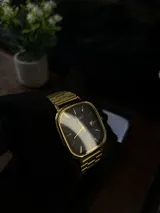 Reloj Casio Quartz con caja cuadrada y correa de eslabones en tono dorado. La esfera es de color negro con manecillas y marcadores de hora dorados, y cuenta con una ventana de fecha.