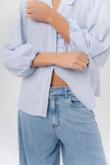 Camisa de manga larga color beige con diseño a rayas sutiles, cuello mao con volados y abertura frontal con detalles de volados a un lado.