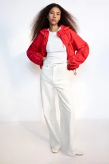 Chaqueta corta de nylon color beige, con cuello subido, capucha y cierre frontal con cremallera. Presenta mangas largas con puños elásticos, bolsillos laterales y detalles de cordones ajustables con lazadas en el pecho y el bajo.