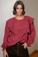Blusa blanca de algodón con cuello redondo, mangas largas con puños elásticos y volados decorativos en los hombros.