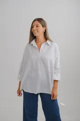 Blusa de corte holgado con estampado de rayas verticales azules sobre fondo blanco. Presenta cuello camisero con escote en V y mangas largas amplias con puños vueltos.