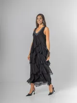 Vestido largo negro de seda con escote en V adornado con lentejuelas plateadas. Presenta un diseño de capas superpuestas con terminaciones deshilachadas que aportan volumen y movimiento. Es de corte sin mangas con breteles anchos y espalda elastizada.