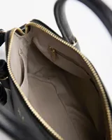 Cartera chica tipo bolso de mano XL Extra Large de color negro, confeccionada en material sintético con textura granulada. Cuenta con doble asa corta superior, herrajes dorados, detalles de tiras colgantes decorativas y correa ajustable y desmontable para usar cruzada o al hombro.