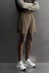 Short de running 2 en 1 color beige, confeccionado en tejido técnico ligero y elástico con malla interior integrada. Presenta cintura elástica ajustable con cordón, bolsillo trasero con cierre y aberturas laterales en el bajo.