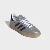 Championes Adidas Handball Spezial de caña baja, con exterior de cuero sintético metalizado color plata y tres franjas laterales negras. Presentan detalles en negro en el talón y cuello, cordones blancos y suela de caucho color caramelo.