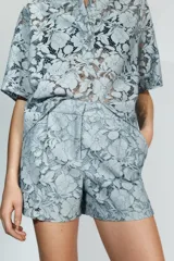 Shorts de tiro alto confeccionados en encaje con diseño floral. Presentan bolsillos delanteros y cierre frontal con cremallera y gancho metálico.