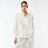 Camisa de lino mezclado color blanco con rayas verticales oscuras, cuello camisero, manga larga y cierre frontal con botones.