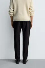 Pantalón de corte slim fit y color negro, confeccionado en tejido elástico. Cuenta con cintura elástica, trabillas, bolsillos frontales y cierre con cremallera y botón.