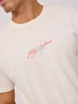 Remera negra de algodón con estampado en la espalda con palmeras, tabla de surf y texto en color blanco y fucsia.