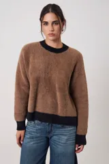 Sweater de tejido suave con textura peluda, de corte holgado y manga larga. Presenta un diseño bicolor con cuerpo en tono beige melange y terminaciones en cuello, puños y ruedo en color negro.