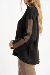 Polera de punto con calce oversize, cuello alto y mangas largas. Presenta un diseño en color negro con franjas laterales en las mangas y detalle en el cuello en tono bronce con acabado brillante.