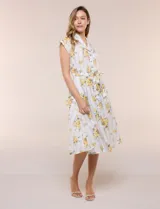 Vestido camisero midi de silueta evasé, confeccionado en tejido liviano blanco con estampado floral amarillo y rayas celestes. Cuenta con cuello solapa en V, cartera con botones frontales, mangas cortas japonesas y cintura definida con lazo ajustable a juego.