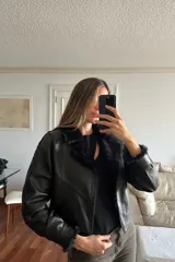 Campera bomber corta de napalan negro con interior forrado en piel sintética color azul noche. Presenta cierre frontal, cuello con solapas y detalles de pasamanería en cruz a lo largo de las mangas.