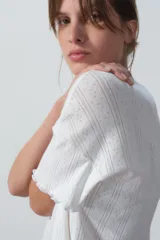 Remera blanca de punto calado con cuello redondo y mangas cortas con terminación ondulada.