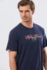 Remera azul marino de manga corta con cuello redondo, confeccionada en mezcla de algodón y poliéster. Presenta un diseño en el frente que combina estampa y bordado con la leyenda "Legacy Brand 1972" en tonos rosado, verde y marrón.