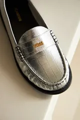 Mocasines negros de cuero con textura croco y detalle de logo VDM en dorado.