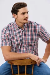 Camisa de manga corta con estampado de cuadros en tonos azules, rojos y blancos, cuello con botones y bolsillo ojal en el pecho con logo bordado.