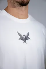 Remera de corte oversize color blanco, con cuello redondo y mangas cortas. Presenta un pequeño estampado gráfico central en el pecho con diseño de querubín con alas.